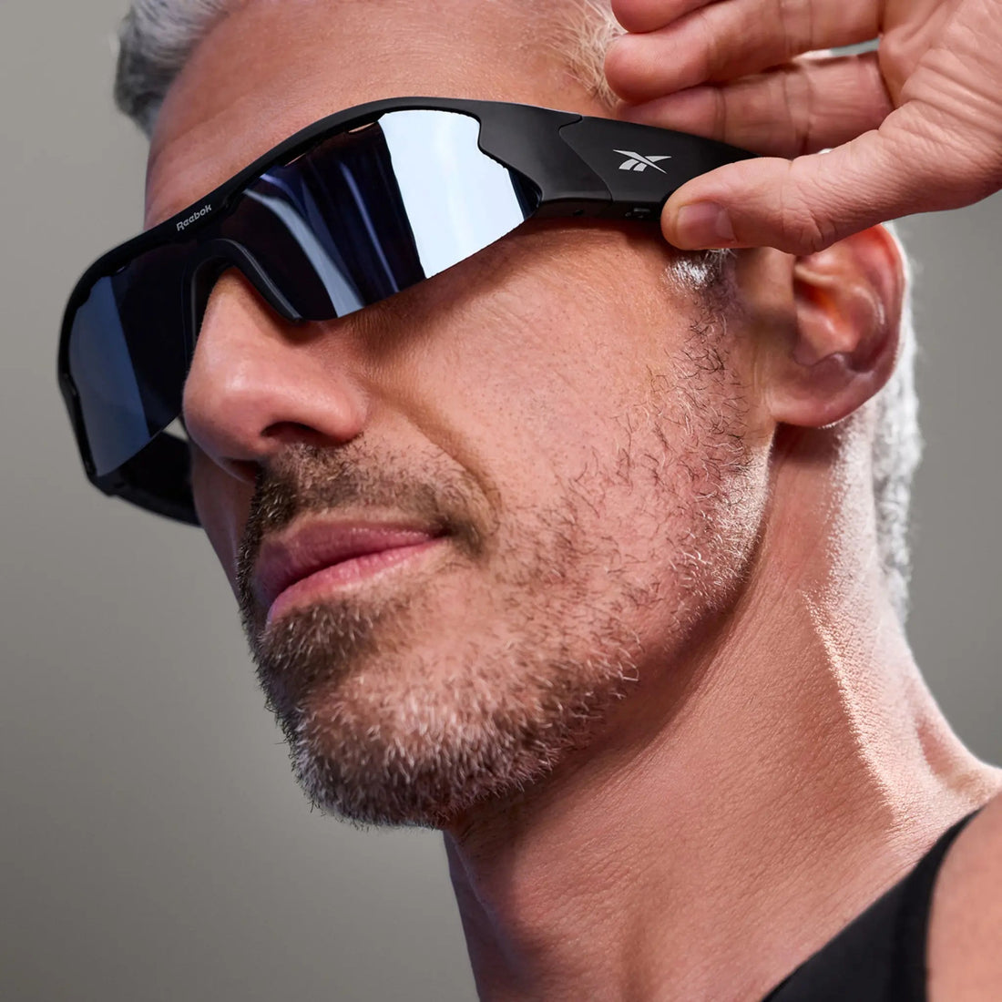 Model wearing Reebok Octane Silver Mirror smart sunglasses and touching the side arm.